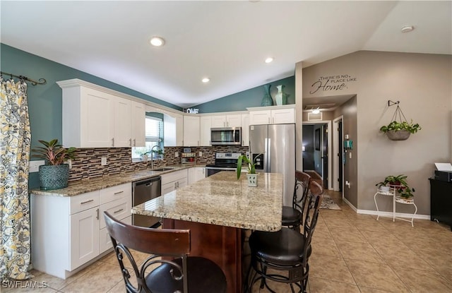 kitchen featuring a center island, white cabinets, vaulted ceiling, decorative backsplash, and appliances with stainless steel finishes