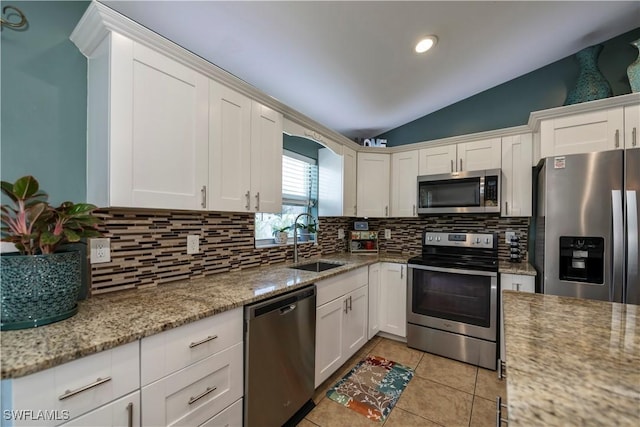 kitchen featuring appliances with stainless steel finishes, light stone counters, vaulted ceiling, sink, and white cabinetry