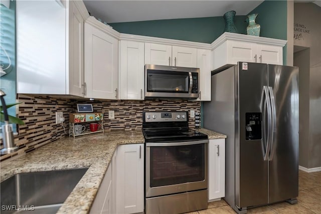 kitchen with lofted ceiling, white cabinets, light stone countertops, light tile patterned floors, and stainless steel appliances