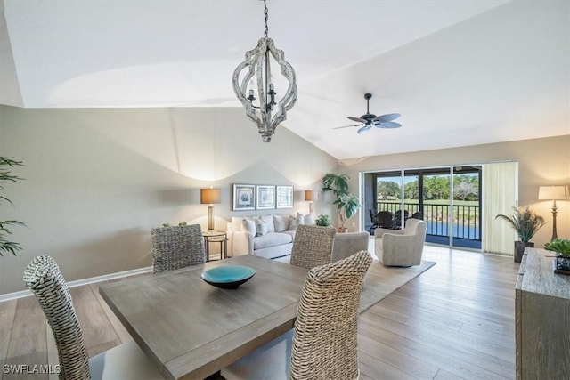 dining room with ceiling fan with notable chandelier, light wood-type flooring, and vaulted ceiling