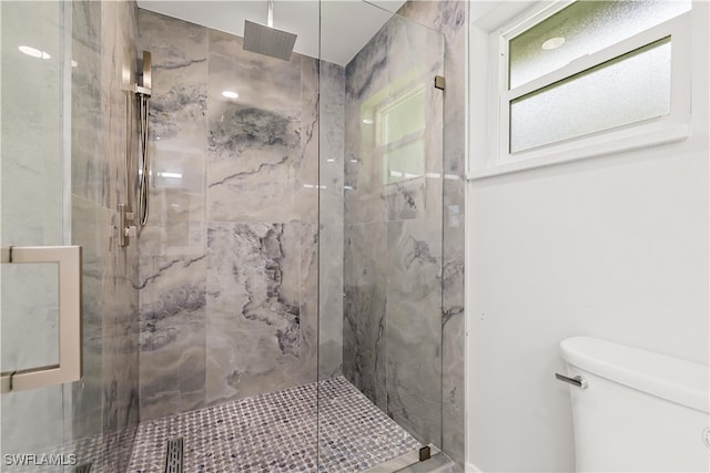 bathroom featuring a shower with door and toilet