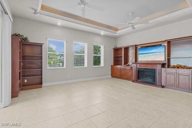 unfurnished living room with light tile patterned floors, baseboards, a fireplace with raised hearth, a raised ceiling, and a ceiling fan