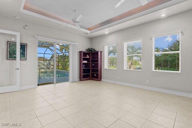 tiled empty room with a tray ceiling, ceiling fan, and plenty of natural light