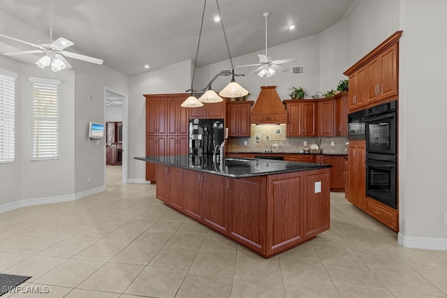 kitchen featuring dark stone counters, black appliances, premium range hood, an island with sink, and ceiling fan