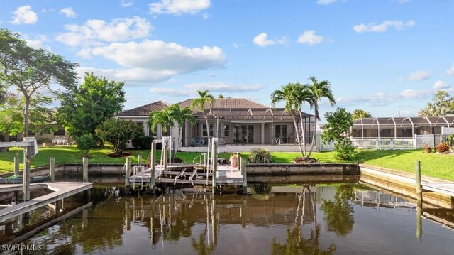 view of dock with a water view, a lawn, and glass enclosure