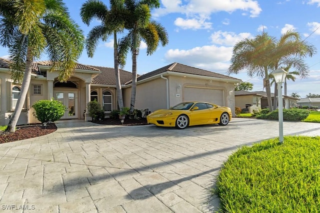 mediterranean / spanish home with decorative driveway, a tile roof, french doors, stucco siding, and a garage