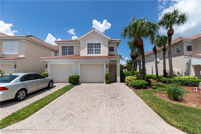 mediterranean / spanish home with a garage, a tile roof, decorative driveway, and stucco siding