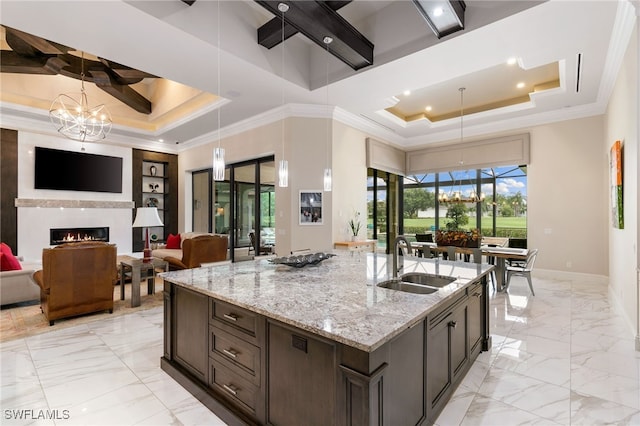 kitchen featuring a tray ceiling, light stone counters, sink, and dark brown cabinets