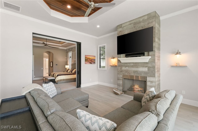 living room featuring a tray ceiling, crown molding, light hardwood / wood-style flooring, and a high end fireplace