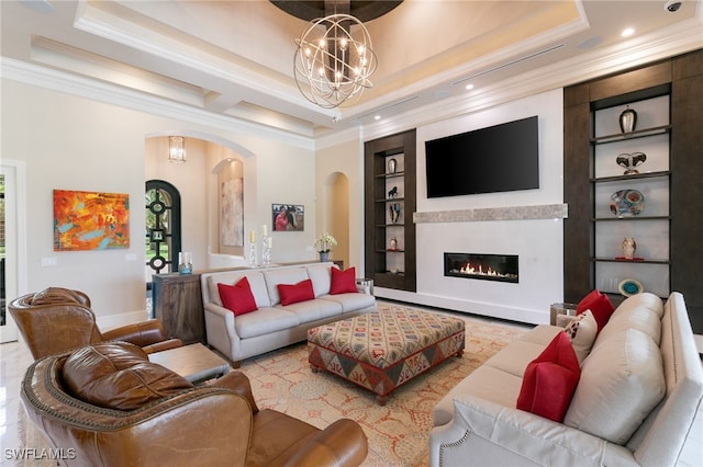 living room with a chandelier, built in shelves, a tray ceiling, and ornamental molding