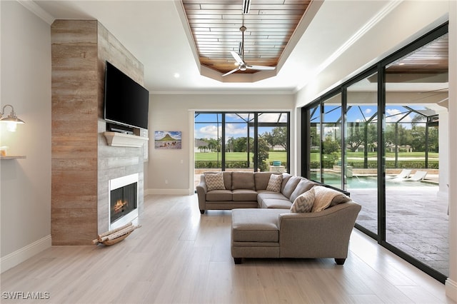 living room with a raised ceiling, light wood-type flooring, crown molding, and a tiled fireplace