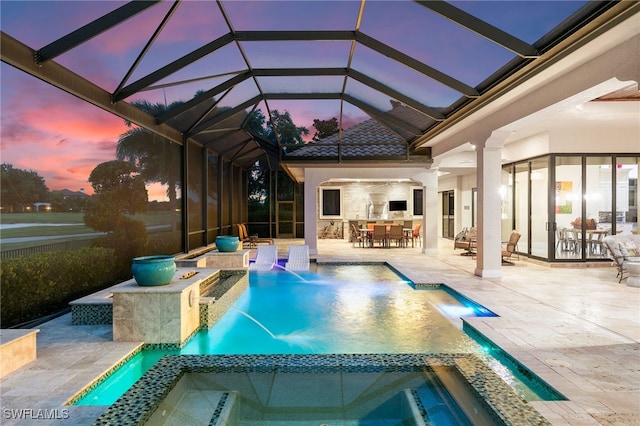 pool at dusk with an in ground hot tub, a patio, pool water feature, and a lanai