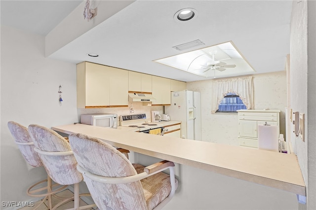 kitchen with ceiling fan, kitchen peninsula, cream cabinets, white appliances, and a breakfast bar area