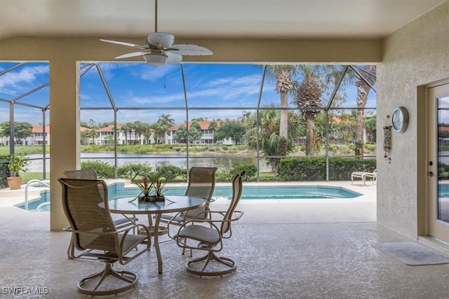 view of pool featuring a patio area, ceiling fan, glass enclosure, and a water view