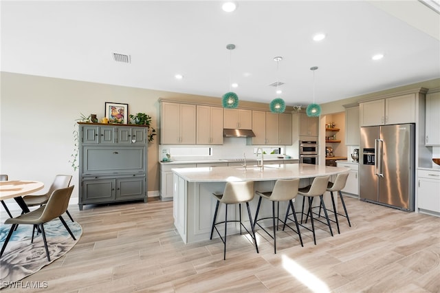 kitchen with a kitchen island with sink, hanging light fixtures, light hardwood / wood-style flooring, gray cabinets, and appliances with stainless steel finishes