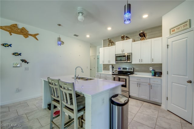 kitchen with a kitchen island with sink, white cabinets, sink, hanging light fixtures, and stainless steel appliances