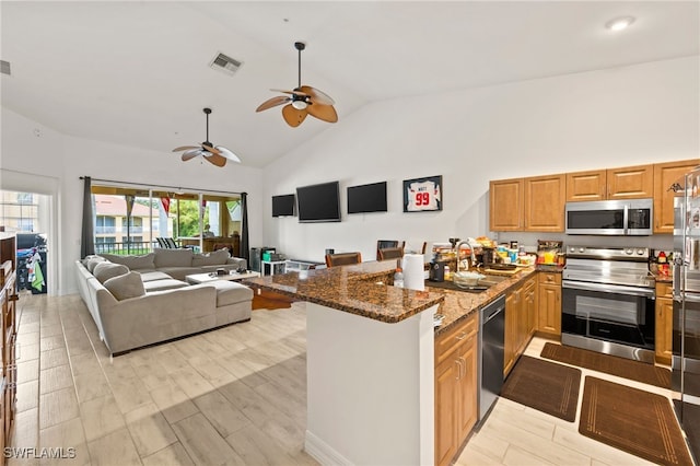 kitchen with dark stone counters, sink, light hardwood / wood-style flooring, ceiling fan, and stainless steel appliances