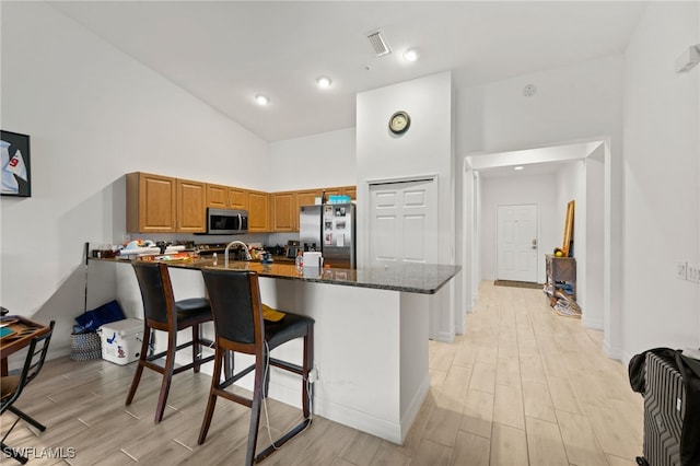 kitchen featuring stainless steel appliances, light hardwood / wood-style floors, high vaulted ceiling, dark stone counters, and kitchen peninsula