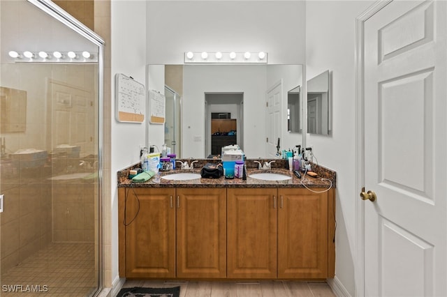 bathroom with hardwood / wood-style floors, dual bowl vanity, and a shower with shower door