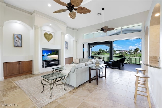 living room with ceiling fan, decorative columns, and a towering ceiling