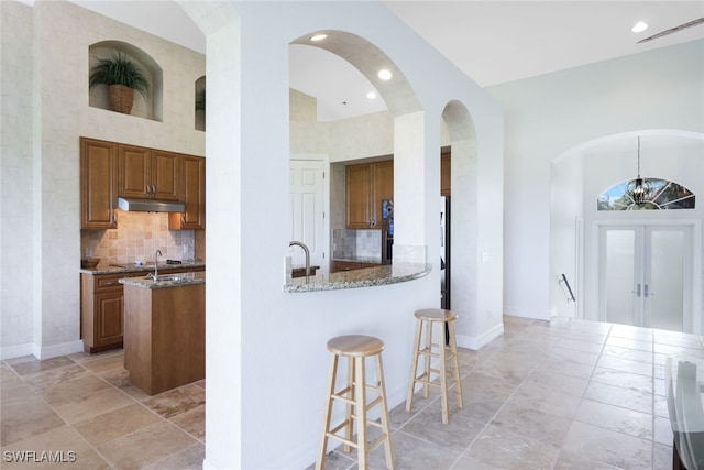 kitchen featuring stone counters, a breakfast bar, tasteful backsplash, a high ceiling, and kitchen peninsula