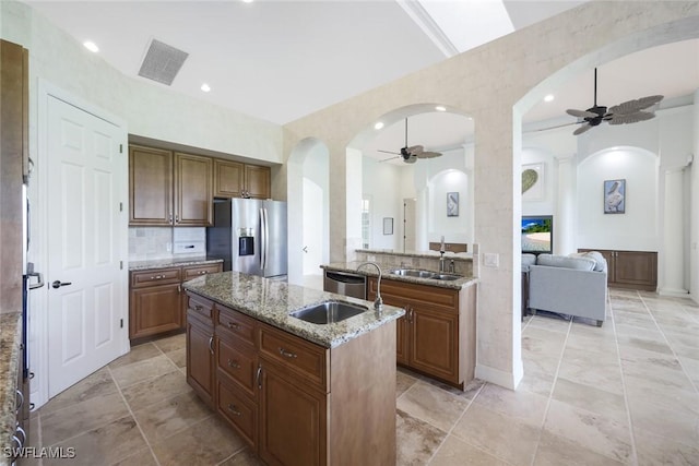 kitchen featuring stainless steel refrigerator with ice dispenser, sink, light stone countertops, and an island with sink