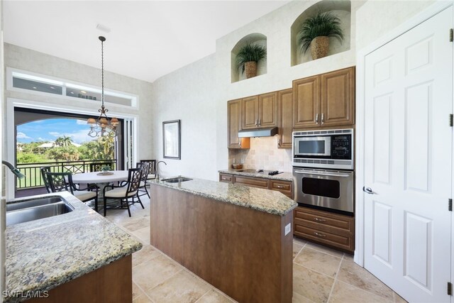 kitchen with sink, appliances with stainless steel finishes, light stone countertops, an island with sink, and decorative light fixtures