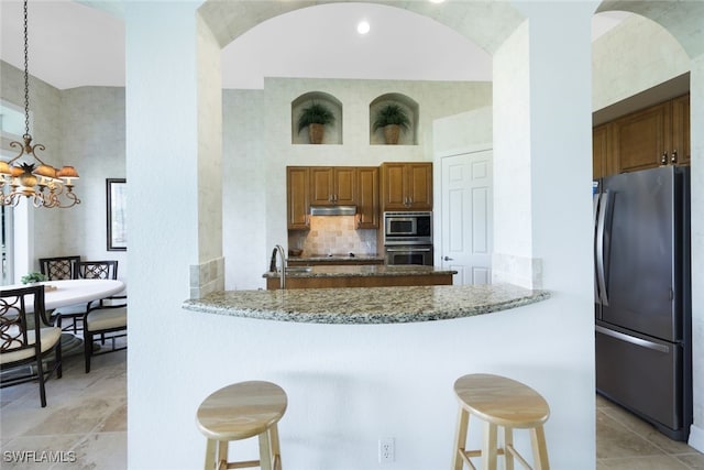 kitchen with appliances with stainless steel finishes, kitchen peninsula, decorative light fixtures, light stone counters, and a breakfast bar area