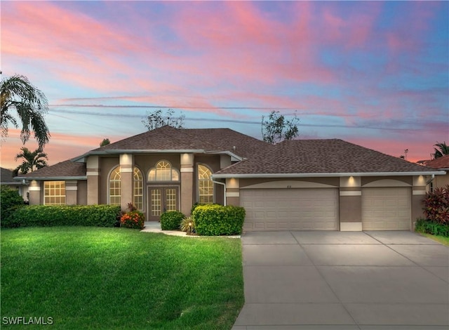 view of front of property featuring driveway, a yard, stucco siding, french doors, and a garage