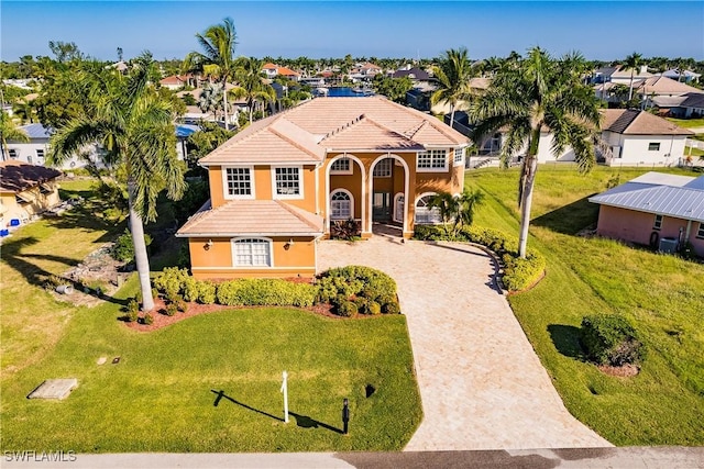 mediterranean / spanish-style home featuring a tile roof, driveway, a residential view, stucco siding, and a front lawn