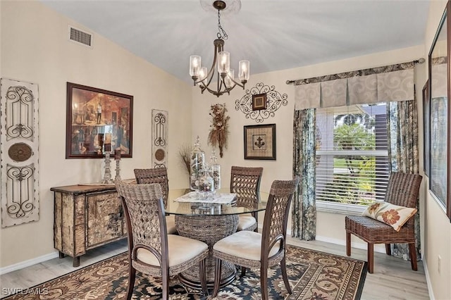 dining space with light wood finished floors, visible vents, baseboards, a chandelier, and lofted ceiling