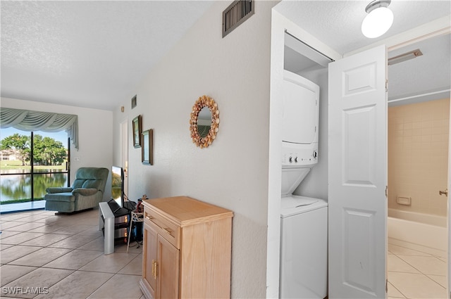 corridor featuring light tile patterned floors, stacked washer / dryer, and a textured ceiling