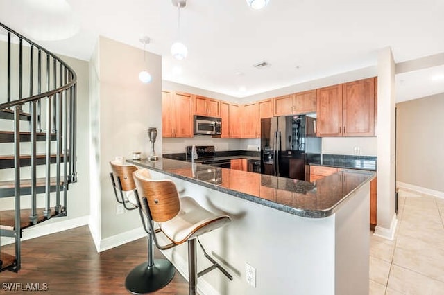 kitchen featuring range with electric cooktop, decorative light fixtures, a kitchen bar, kitchen peninsula, and black fridge