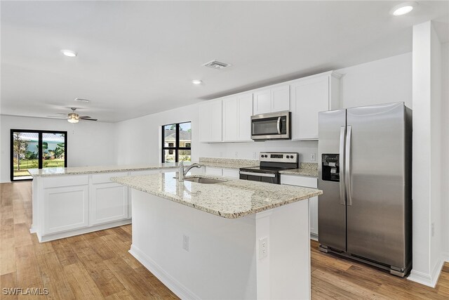 kitchen with sink, stainless steel appliances, light hardwood / wood-style floors, and a kitchen island with sink