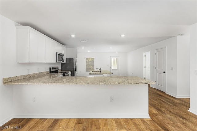 kitchen featuring light stone counters, stainless steel appliances, white cabinetry, wood finished floors, and a peninsula