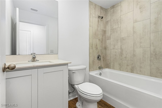 full bathroom featuring hardwood / wood-style floors, tiled shower / bath combo, vanity, and toilet