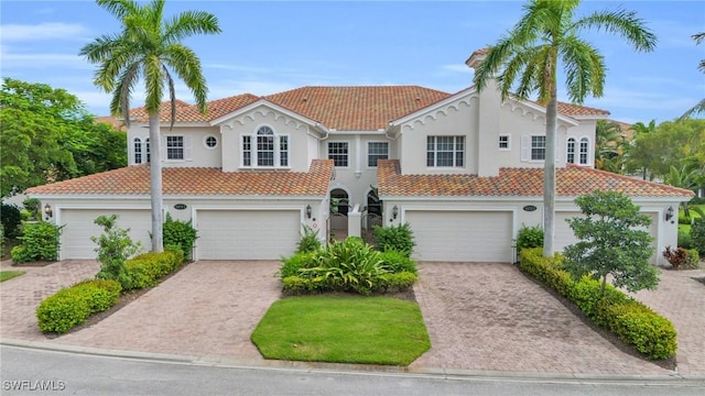 mediterranean / spanish house featuring a garage, decorative driveway, a tiled roof, and stucco siding