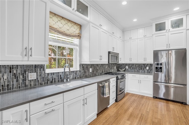 kitchen with appliances with stainless steel finishes, sink, light hardwood / wood-style flooring, and backsplash