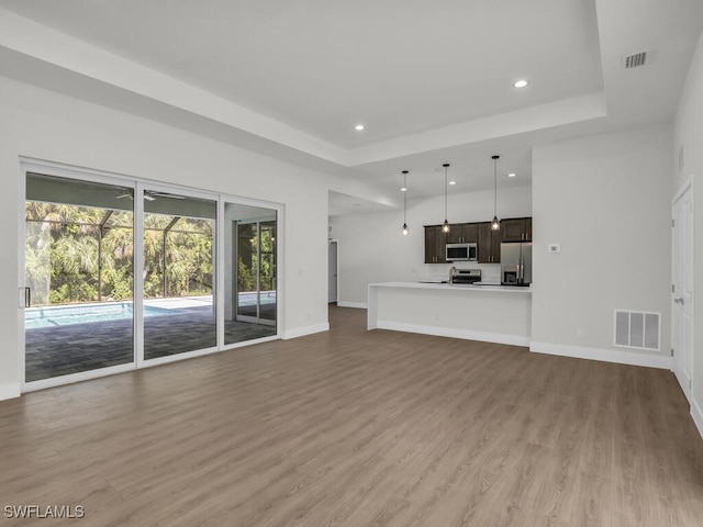 unfurnished living room featuring a raised ceiling, sink, and hardwood / wood-style floors