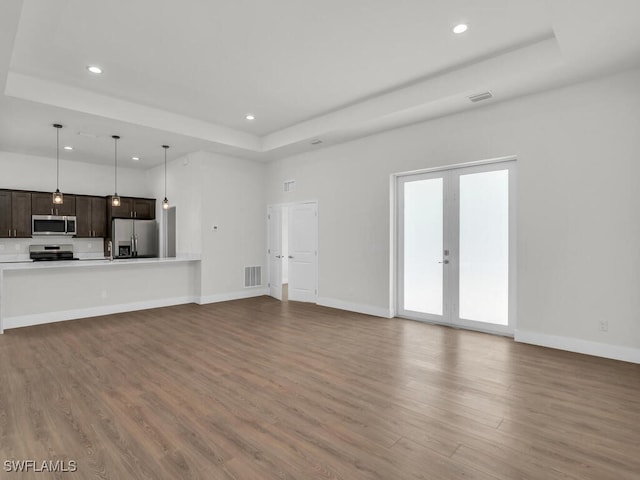 unfurnished living room with french doors, a raised ceiling, and hardwood / wood-style floors