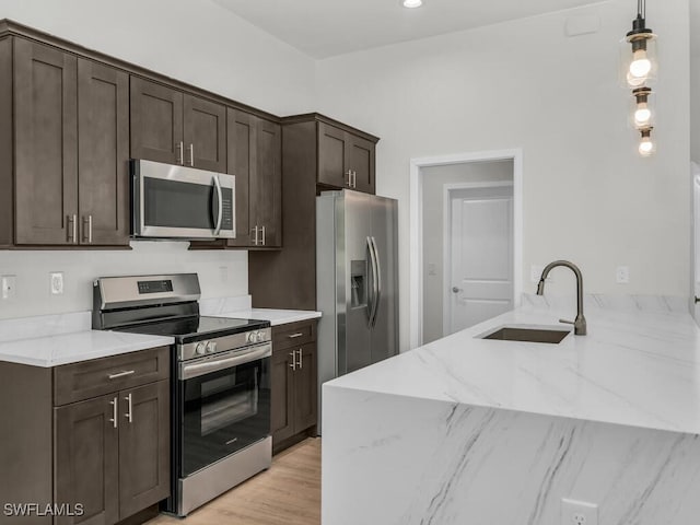 kitchen featuring hanging light fixtures, light stone counters, sink, light hardwood / wood-style floors, and stainless steel appliances