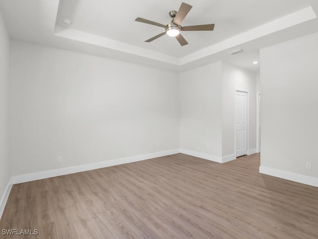 empty room featuring a tray ceiling, light wood-type flooring, and ceiling fan