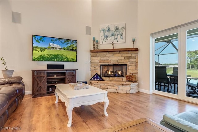 living room featuring light wood-type flooring, a high ceiling, baseboards, and a stone fireplace