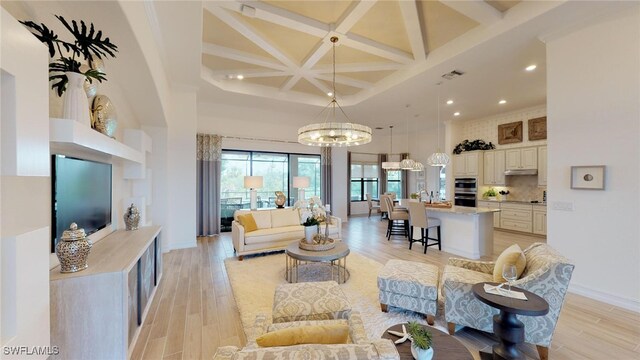 living room featuring coffered ceiling, a notable chandelier, light wood-type flooring, a high ceiling, and beamed ceiling