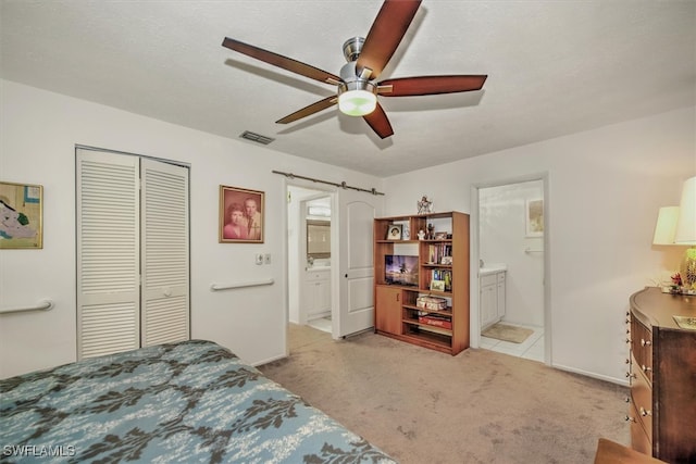 carpeted bedroom featuring ceiling fan, ensuite bath, a barn door, and a closet