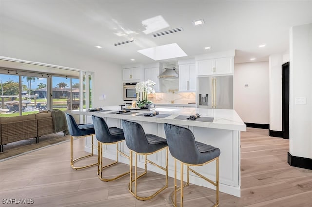 kitchen with a skylight, white cabinets, stainless steel fridge with ice dispenser, a kitchen island, and a breakfast bar