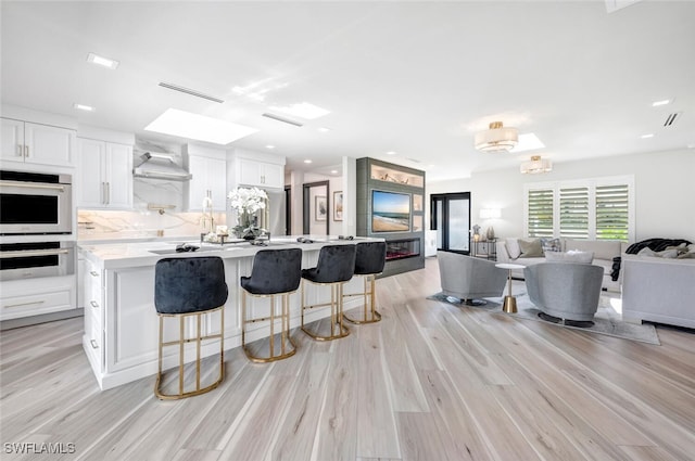 kitchen with light wood-style flooring, white cabinets, open floor plan, light countertops, and backsplash