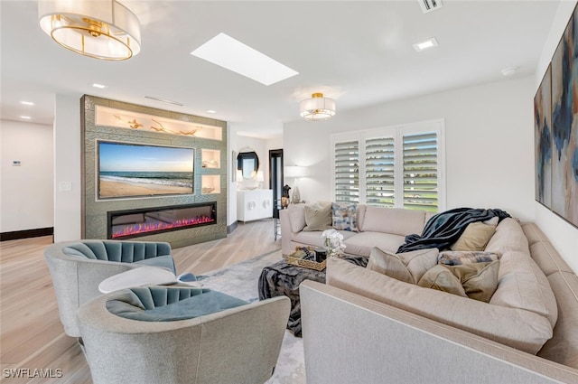 living room with a large fireplace, a skylight, and light wood-type flooring