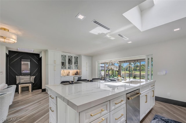 kitchen with an island with sink, dishwasher, light stone countertops, light hardwood / wood-style floors, and white cabinetry