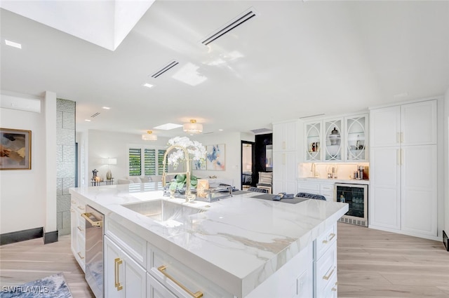 kitchen featuring beverage cooler, visible vents, light stone counters, light wood-style floors, and white cabinetry